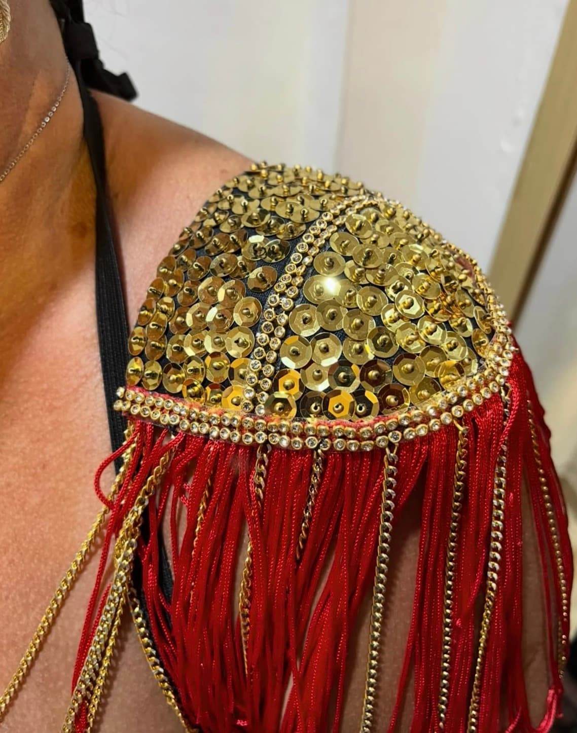Detalhe de peça customizada com paetês dourados e franjas vermelhas
